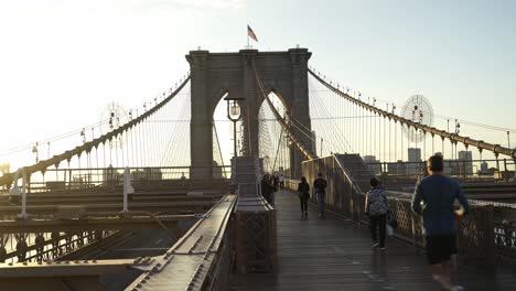 american flag waving on the top of brooklyn bridge with people walking across it