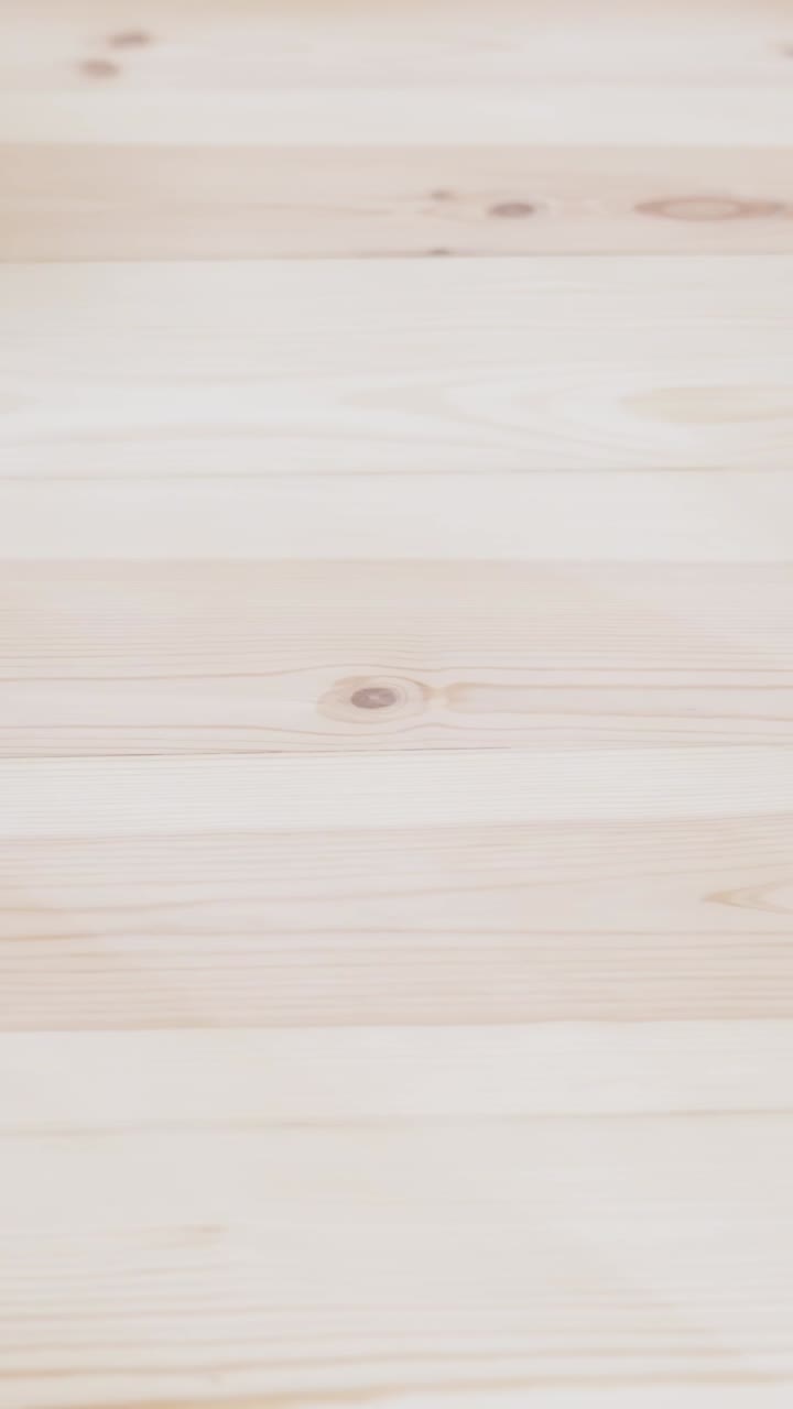Vertical close-up shot of a person's hand using sandpaper on a smooth, light-colored wooden surface, refining the grain in preparation for finishing or restoration work indoors