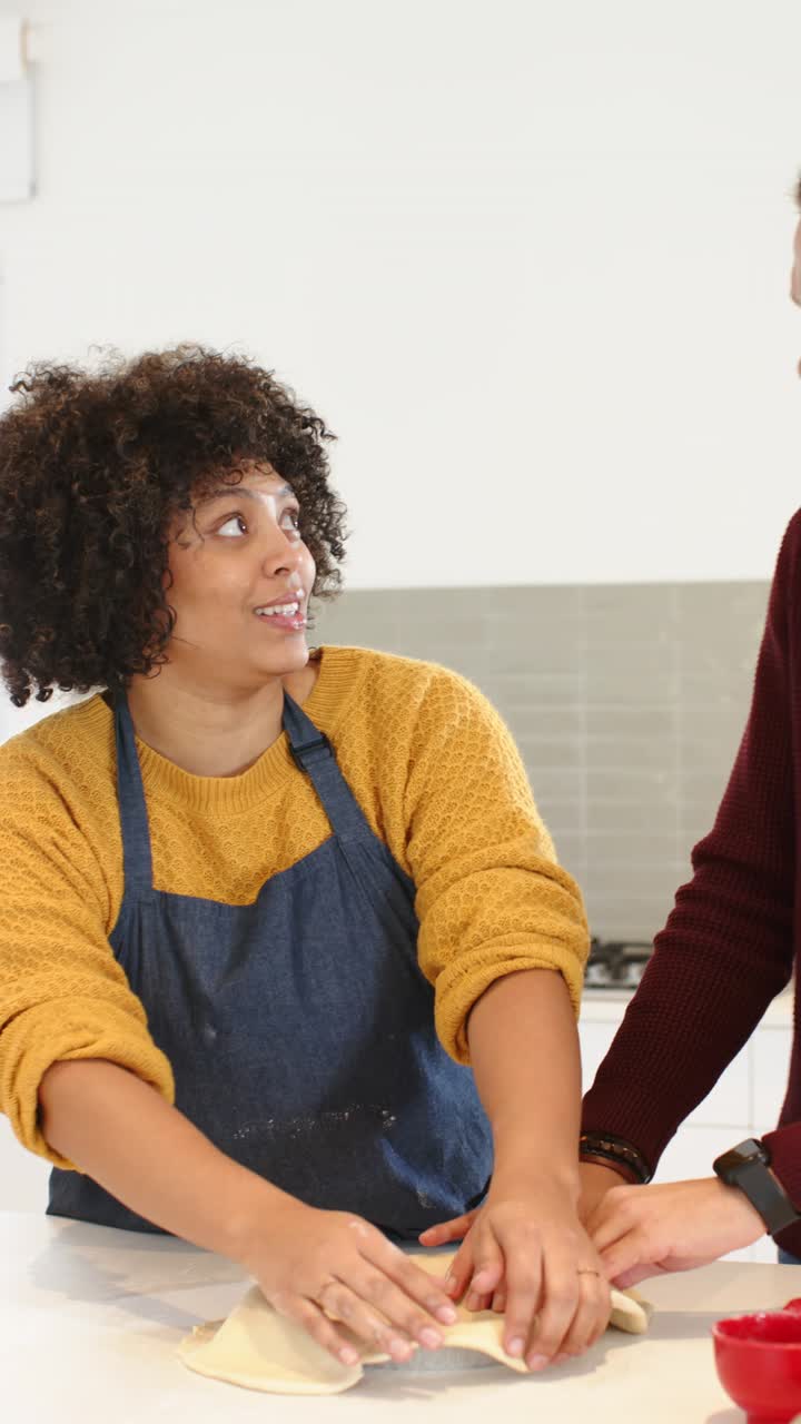 Video verticale: coppia afroamericana che preme la pasta, per poi piegarla sull'isola della cucina per cuocerla in forno
