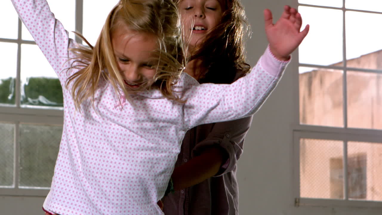 Sisters jumping up and down beside window 