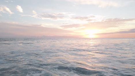 Drone-shot-over-the-white-foaming-waves-of-the-ocean-under-a-beautiful-orange-sunset