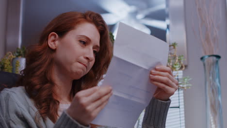 a young caucasian woman opens a letter and receives disappointing news