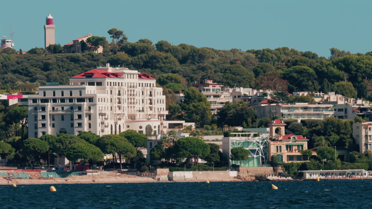 Scenic view of coastal architecture and lighthouse surrounded by trees and hills in Cannes, France