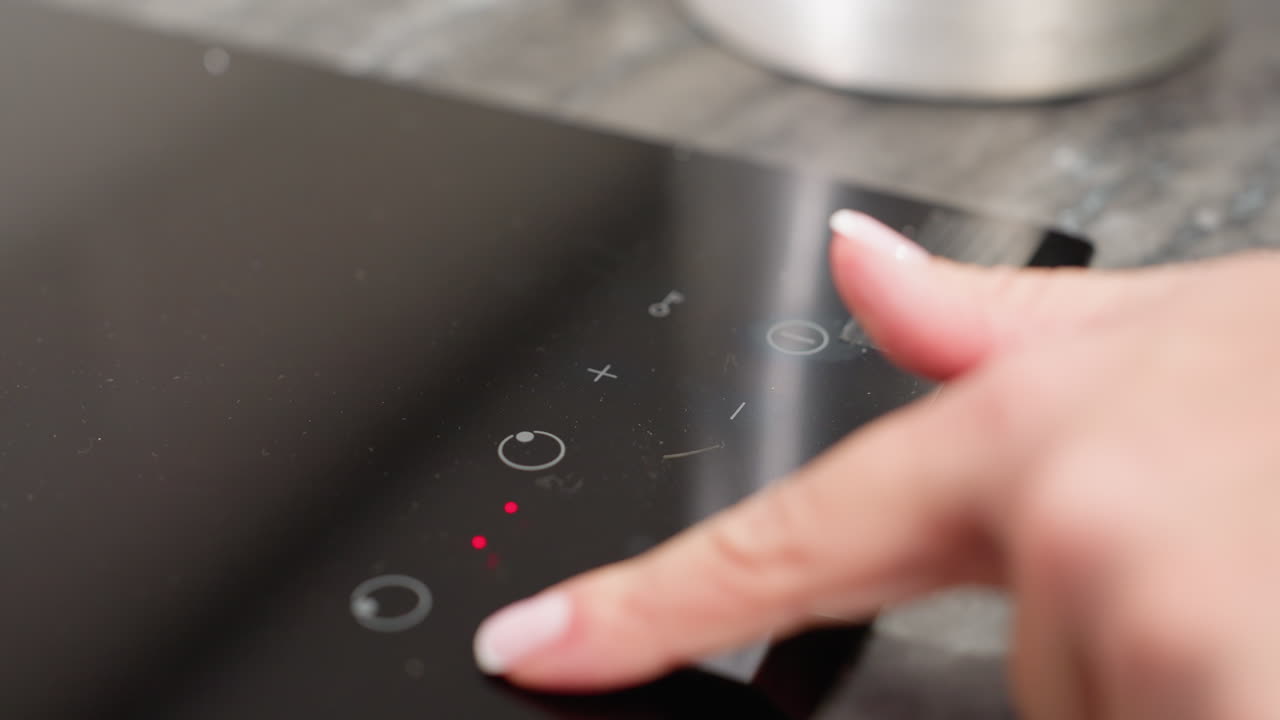 Closeup of female finger pressing power then minus button on modern electric cooker to switch it on and reduce heat level, showcasing smart kitchen technology, and cooking precision