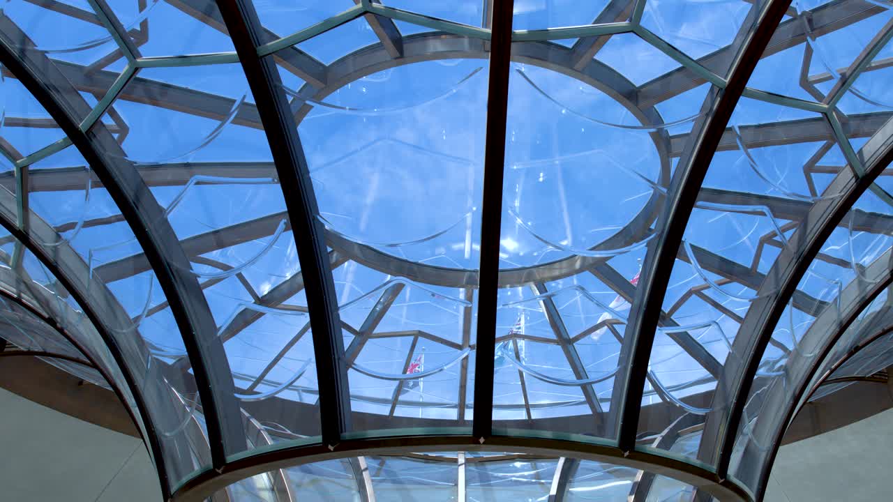 Low angle shot of a geometric glass ceiling dome with blue sky visible through framework