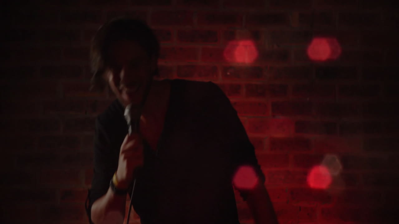 Artista che tiene un microfono con filo sul palco di un locale musicale, mostrando grafici animati di onde sonore rosse.