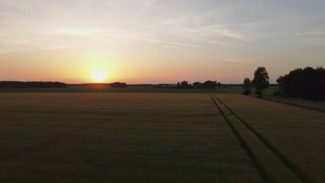 Picturesque-bright-orange-and-yellow-sunset-over-green-farmland,-aerial