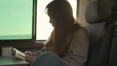 Mujer-Viajera-Leyendo-Un-Libro-En-Una-Camioneta-Al-Atardecer