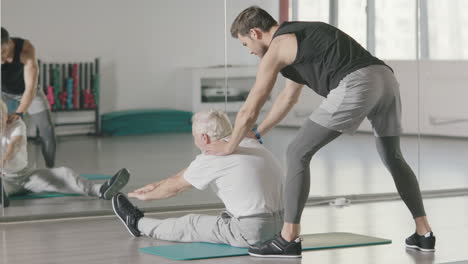 Hombre-Mayor-Haciendo-Ejercicios-De-Estiramiento-Frente-Al-Espejo-En-El-Gimnasio.