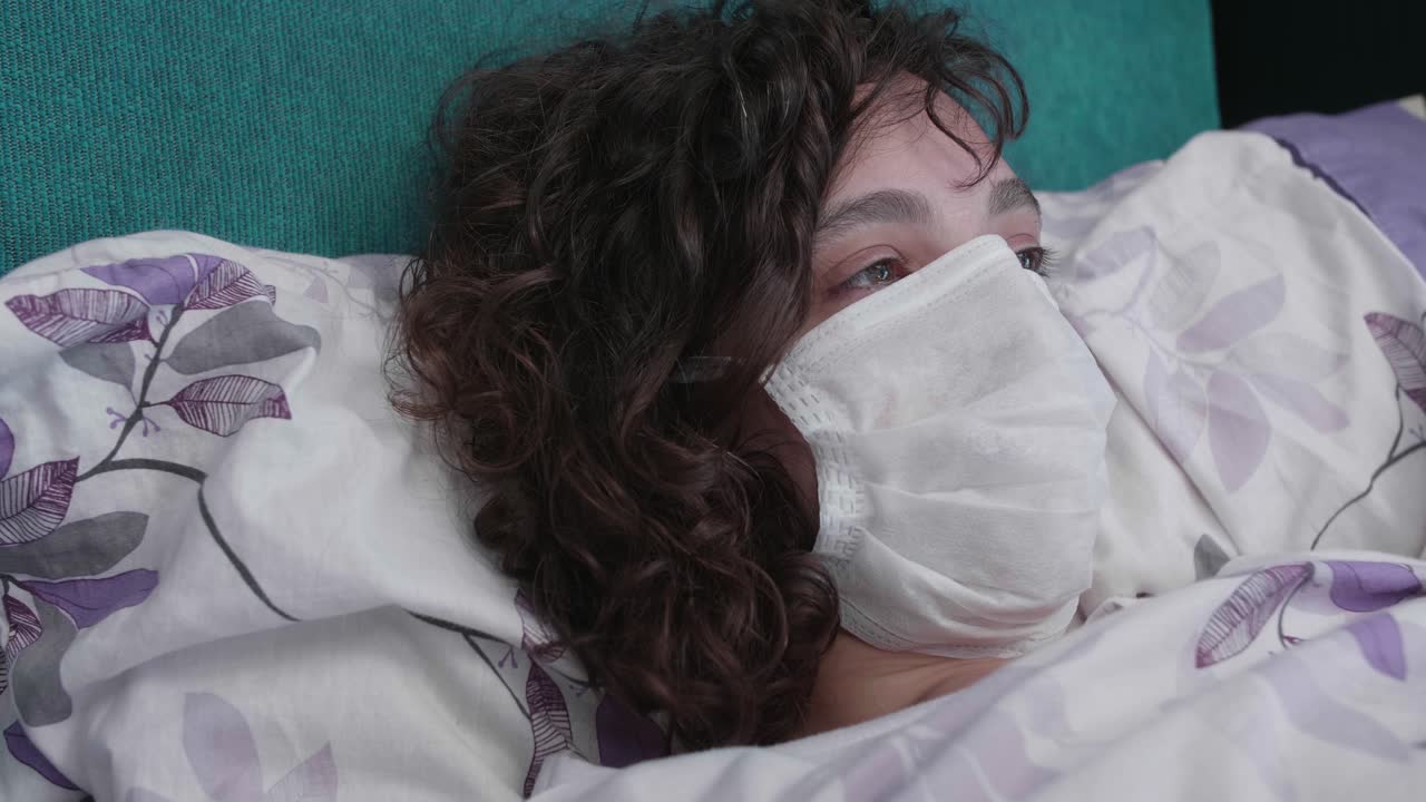 Giovane donna malata che indossa una mascherina medica sdraiata a letto.