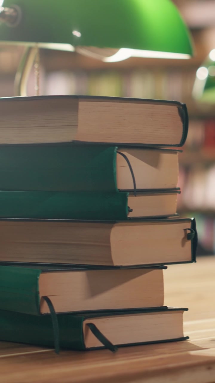 Vertical Video Close up of stacked books on desk in quiet university library with warm lighting