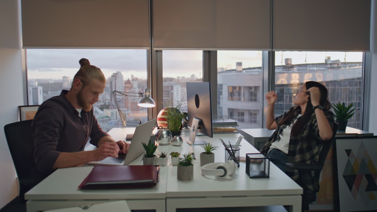 Deadline couple sitting sunset office closeup. Dreaming woman looking window