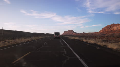 camper van driving down a deserted desert road at sunset