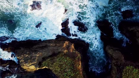 waves crash into a cove eroded out of tall cliffs on the california coast at sunrise