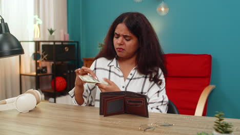 indian woman sad at empty wallet with few money cash bills disappointed financial stress inside home