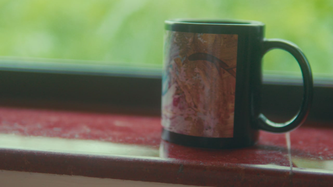 Ceramic mug placed on window ledge with soft natural light and green background calm indoor lifestyle scene