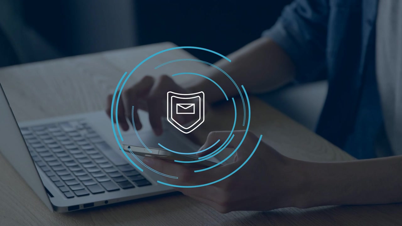 Man hovering over laptop and tapping phone, faint shield with rings forming and securing mail