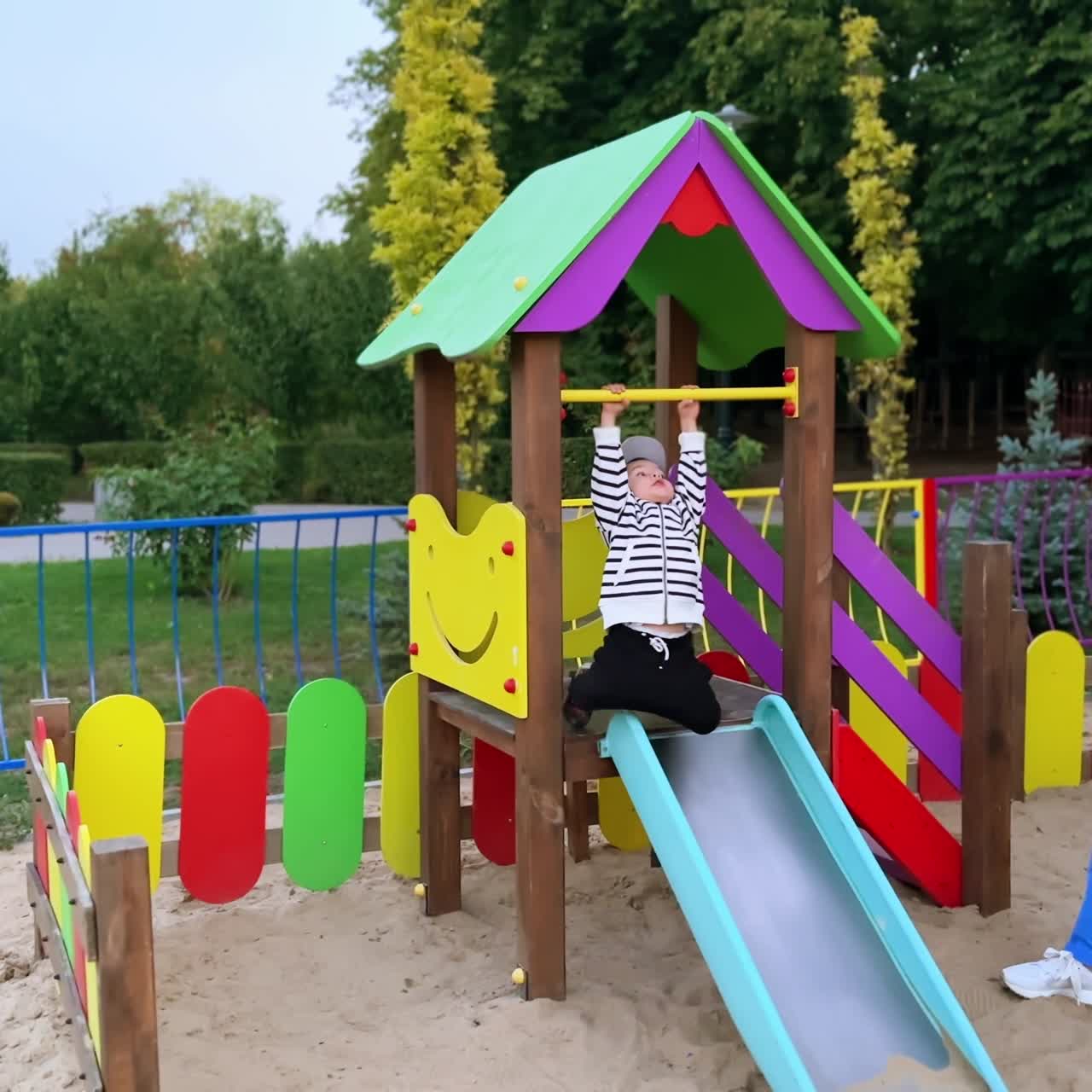 Una madre y su hijo pequeño jugando en el parque. La madre se acerca al niño y le arregla la ropa.