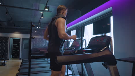 Kaukasischer-Sportler-Joggt-In-Zeitlupe-Auf-Dem-Laufband-In-Einem-Futuristischen-Fitnessstudio,-Hört-Musik,-Trägt-Ein-Tanktop-Und-Schaut-Auf-Den-Fernsehbildschirm---Profilansicht