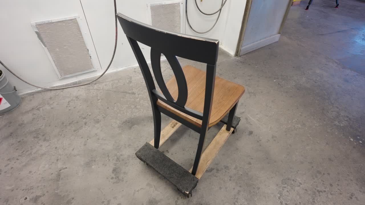 Wide gimbal move shows grey wood dining chair inside an industrial paint booth