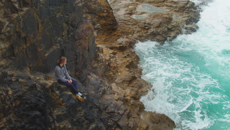 Long-Haired-Caucasian-Lad-Relaxing-In-Rocky-Shore-In-Cornwall,-England-UK