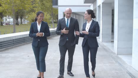 front view of business colleagues walking together at office building, talking and discussing project details