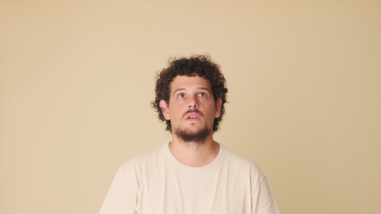 Curly-Haired Man Points Upwards with Surprised and Happy Expression