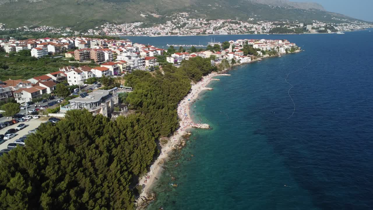 Slow rocket aerial shot of a beach near forest in Split, Croatia, during summer. Beautiful clear turquoise water of the Adriatic sea