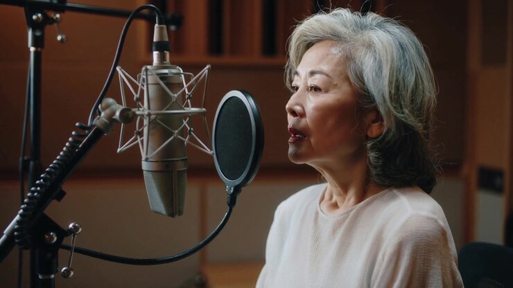Inizio sessione, cantante asiatica con un top rosa che canta in un microfono, con filtro anti-pop, registrando in studio.