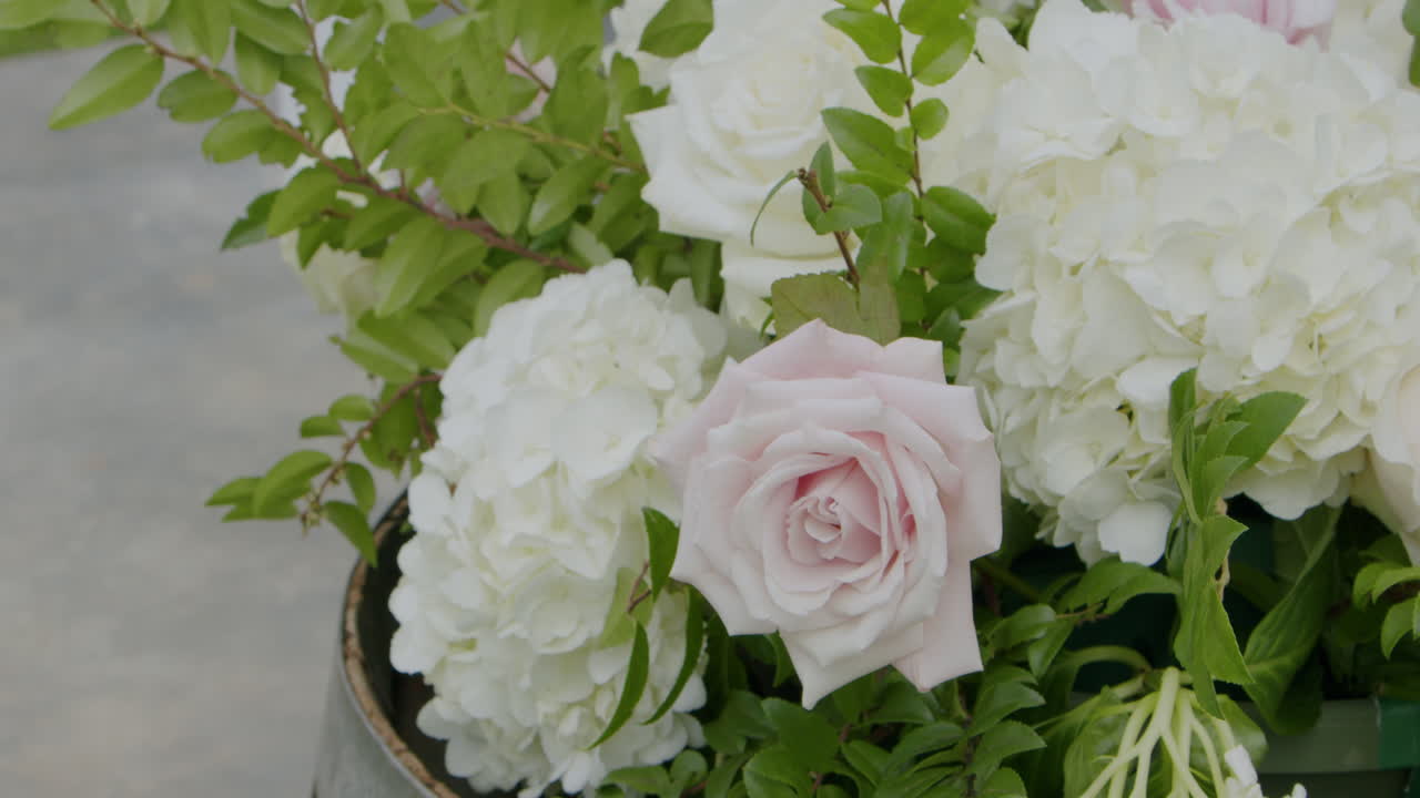 A charming floral arrangement featuring a pink rose sits atop a rustic wood barrel at a wedding, adding a touch of romance and elegance to the outdoor setting.