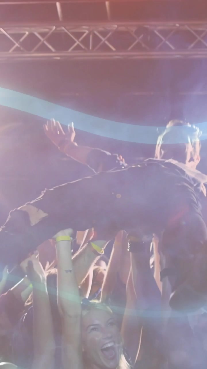 Video verticale: Artista che si protende, la folla lo solleva dal palco coinvolgendo i fan sotto fasci di luce musicale.