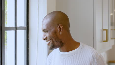 smiling african american man looking out window, enjoying peaceful moment at home