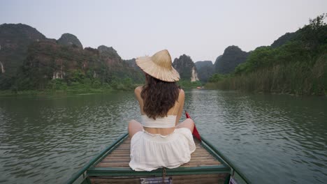 woman in a straw hat sits on a boat in vietnam, surrounded by stunning limestone cliffs