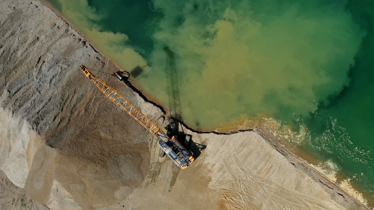 Top down view of an excavator loading sand into the water