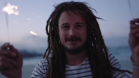 un joven feliz con rastas sosteniendo bengalas celebrando en la playa la víspera de año nuevo