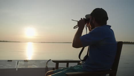 Man-looking-through-binoculars-over-the-flowing-Zambezi-river-searching-for-wild-animals-on-the-river-banks