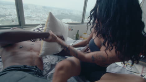 young couple having pillow fight and laughing in bedroom