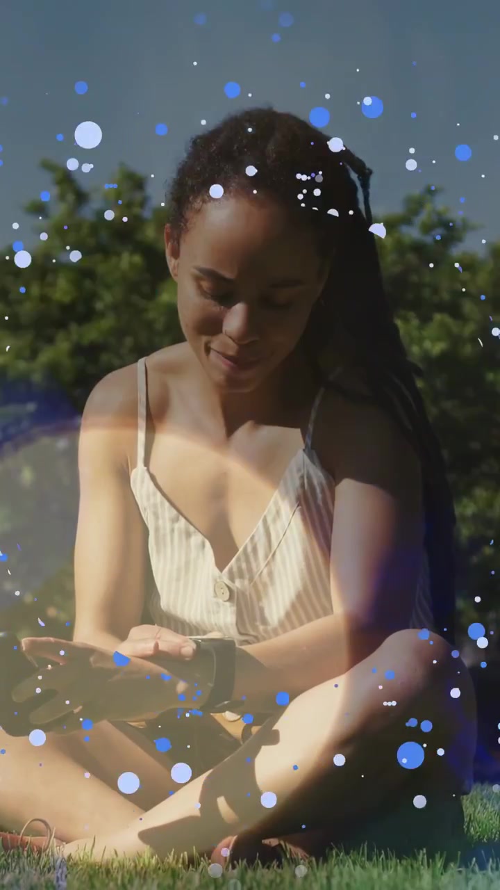 Video verticale: Donna seduta al parco che tocca il telefono e controlla l'orologio, con l'aggiunta di puntini blu per la tecnologia del tempo libero