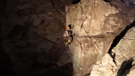 a caver, illuminated by their headlamp, ascends a rugged rock face using single rope technique within the dimly lit anxiety state cave in chiang mai, thailand. the physical exertion and determination.