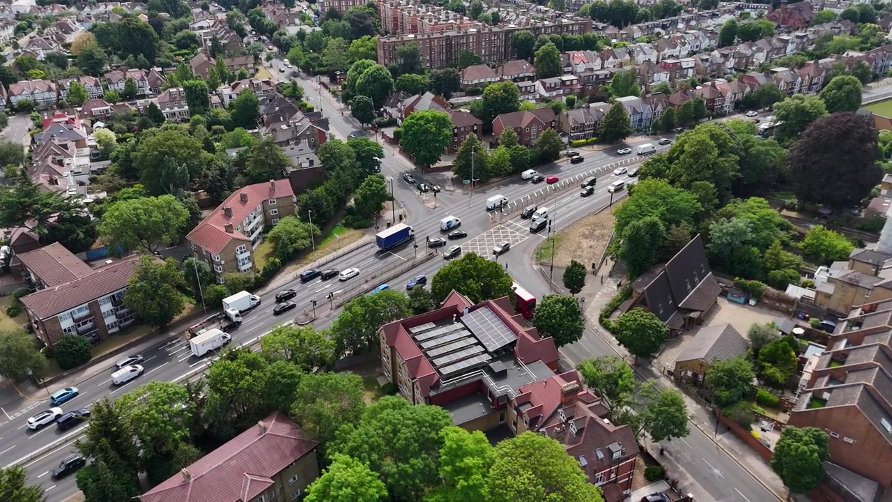 Incrocio stradale con fermata dell'autobus e attraversamento pedonale, situato tra case, appartamenti e alberi maturi in un verde sobborgo di Londra ovest.