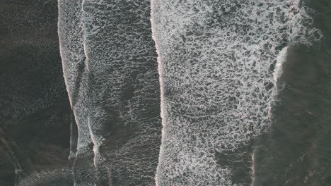 bird's eye aerial rise above gentle waves breaking on remote iceland beach