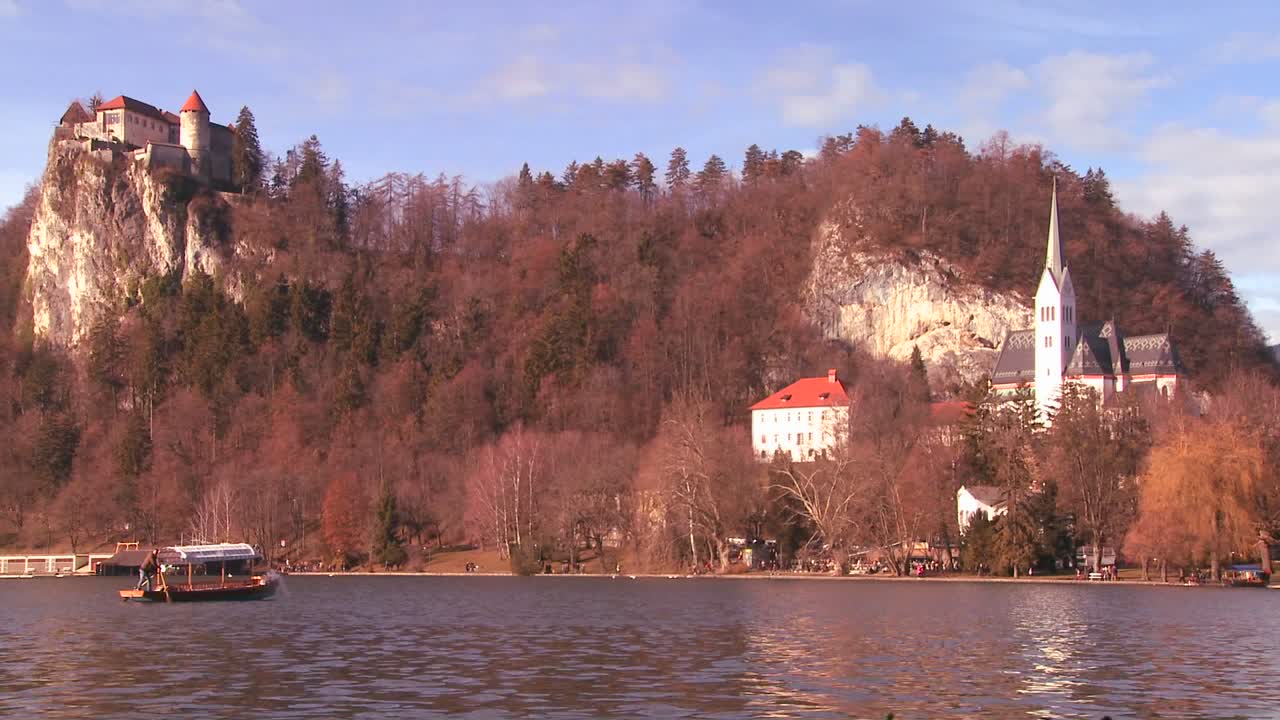 Una barca passa accanto a un bellissimo castello e una chiesa medievale sulle rive del Lago di Bled, Slovenia
