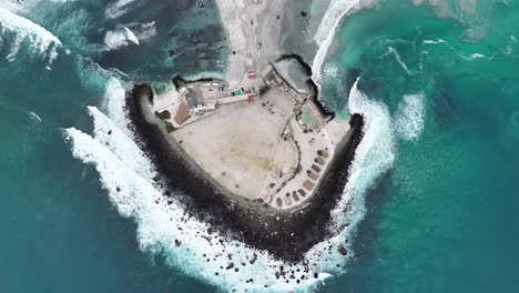 aerial view of a rocky coastal peninsula with buildings and turquoise ocean waves