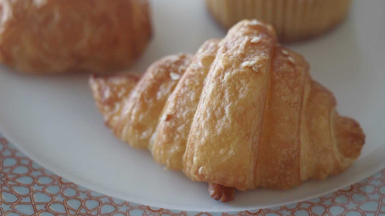 A close-up of croissants on a plate, with a hand reaching to grab one