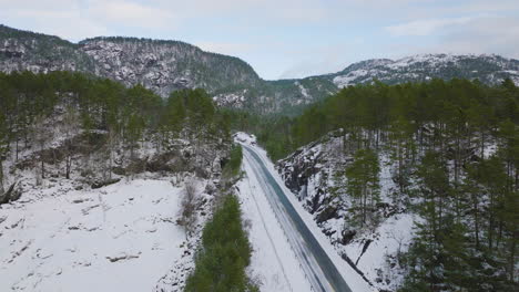 snowy road across norway mountain forest in winter landscape, aerial