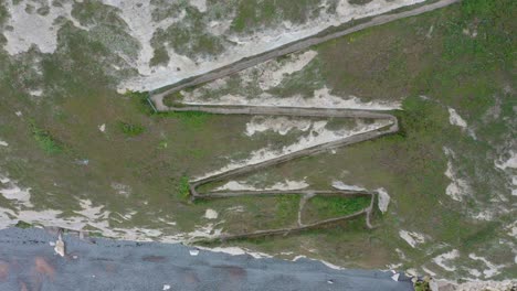 Top-down-aerial-shot-from-cliffside-pathway-to-the-blue-sea-white-cliffs-of-dover