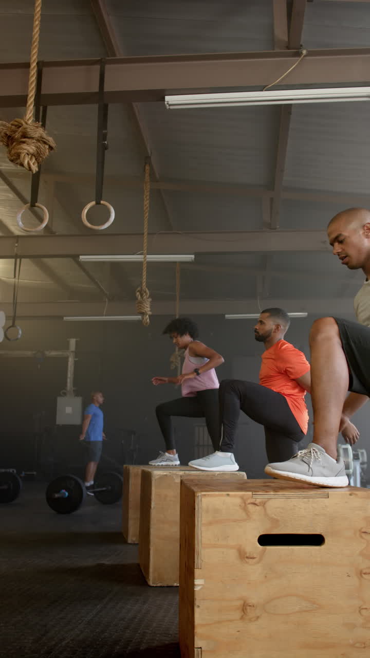 Vertical video of diverse sports people jumping on boxes at gym in slow motion