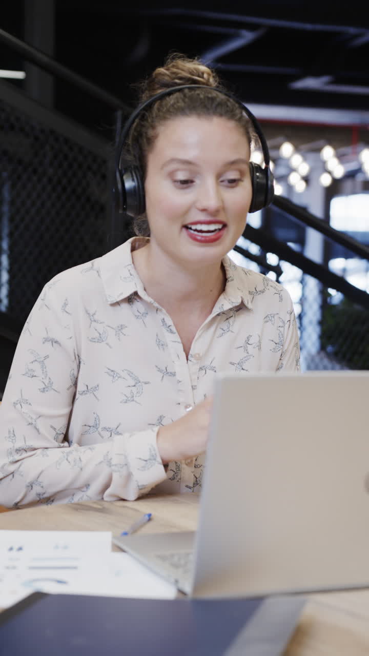 Vertical video of caucasian businesswoman making video call using laptop in casual office