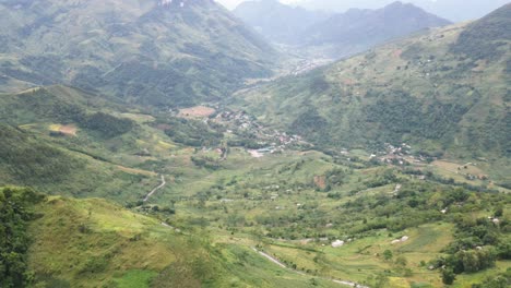 drone flies toward to reveal a huge valley with a small town beneath the mountain range in ha giang viet nam