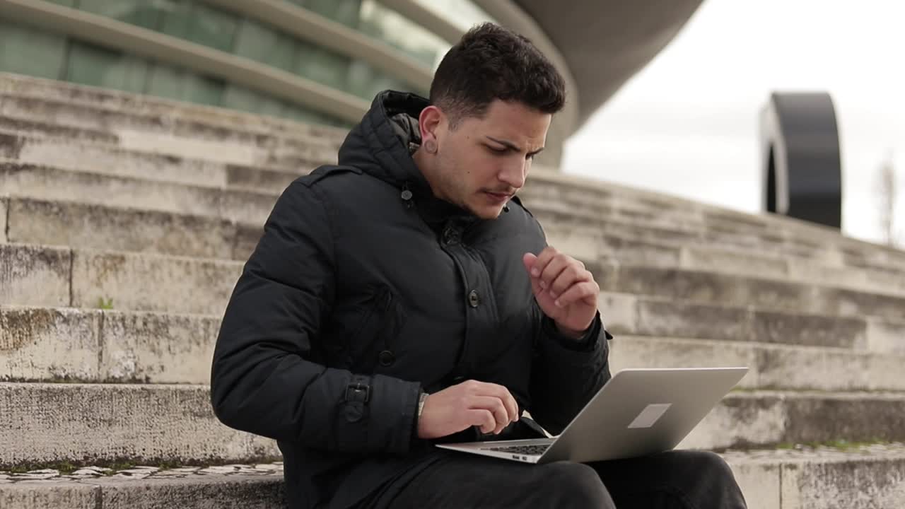 Giovane freelancer concentrato che lavora con il laptop mentre è seduto sulle scale.